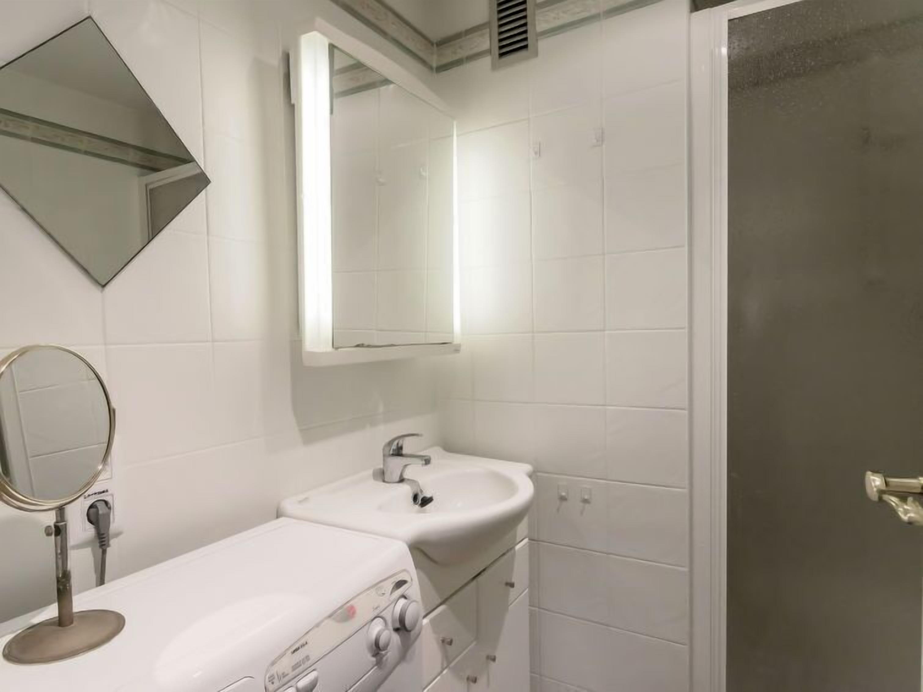 Een badkamer met een witte wastafel, een spiegel en een douchedeur.