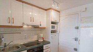 Een compacte keuken met witte kastjes, een ingebouwde oven, een magnetron en een koffiezetapparaat.