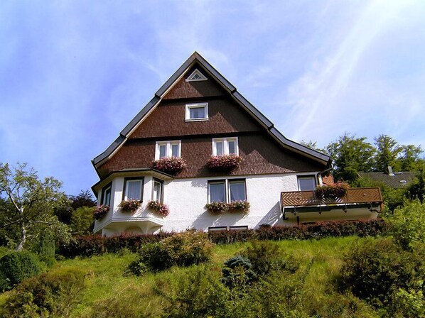 A two-story house with a steeply pitched roof, dormer windows, and flower boxes on the second floor.