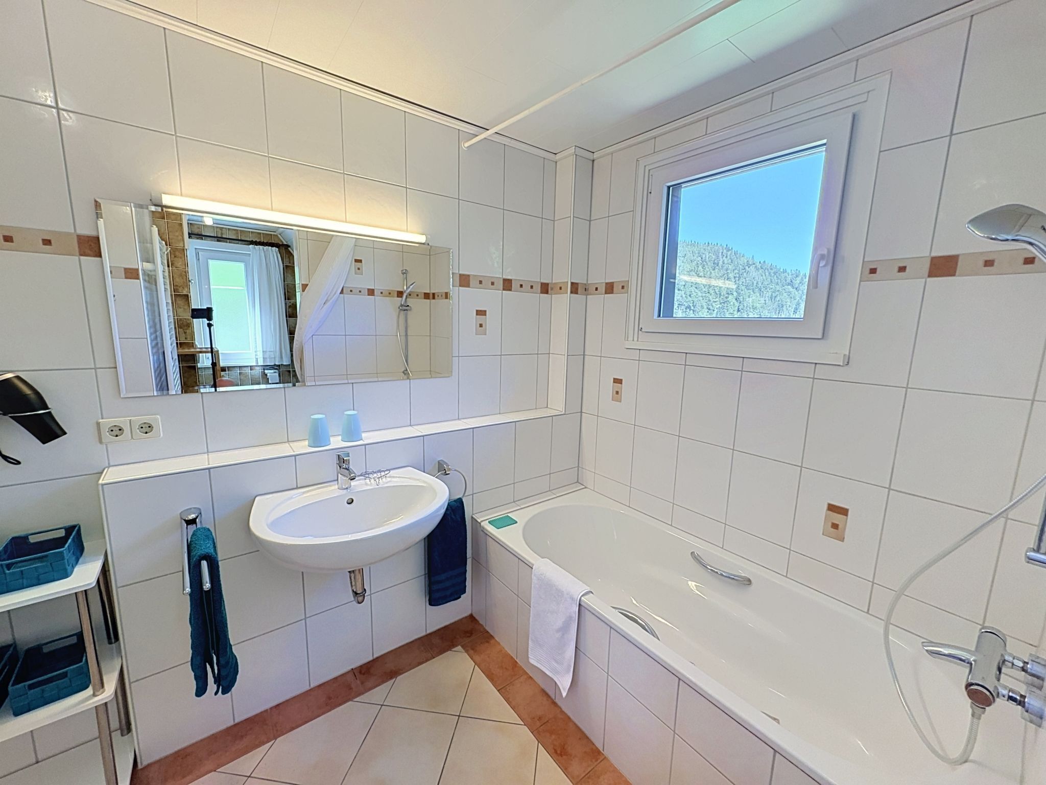 Een moderne badkamer met een wastafel, spiegel, raam en bad.