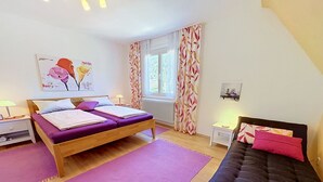 A bedroom with a double bed, a sofa, a desk, and a window with curtains.