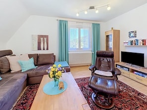 Una sala de estar moderna con un sofá, un sillón de cuero, una mesa baja con flores, un televisor y una estantería.