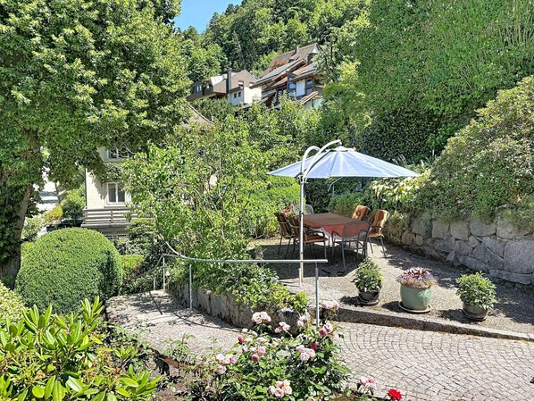 Un patio con un sendero de piedra, una mesa con sillas y plantas en macetas.