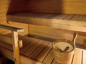 Un banco de madera para sauna con otro banco encima y un balde de madera con una cuchara para servir.