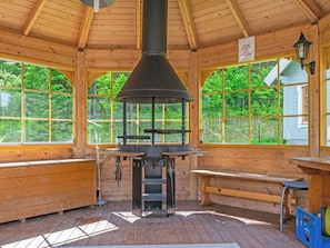 Una cabaña de madera con chimenea central, ventanas amplias y una terraza de madera.