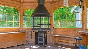 Une cabane en bois dotée d’un poêle à bois central, de grandes fenêtres et d’un banc.