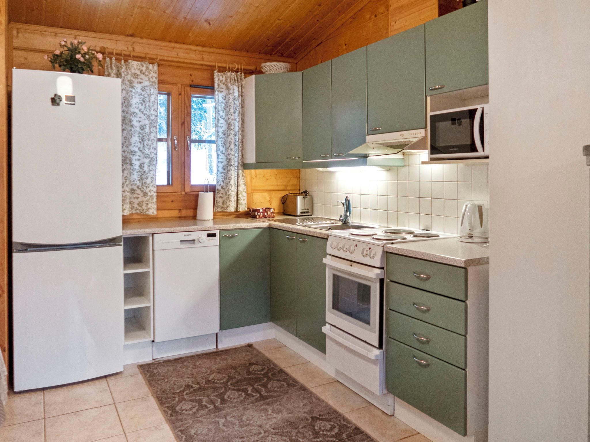 Cocina compacta con refrigerador, lavavajillas, estufa, microondas y una ventana con cortinas.