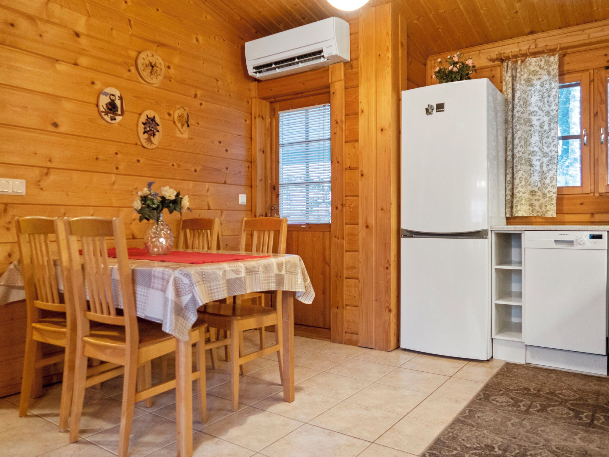 Interior de madera con una mesa de comedor, sillas, un refrigerador y una ventana con persianas.