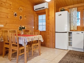 Interior de madera con una mesa de comedor, sillas, un refrigerador y una ventana con persianas.