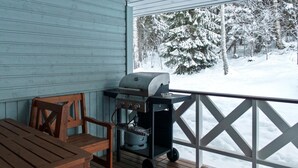 Un espace extérieur abrité, avec une table et des chaises en bois, un barbecue et une vue sur un paysage enneigé.