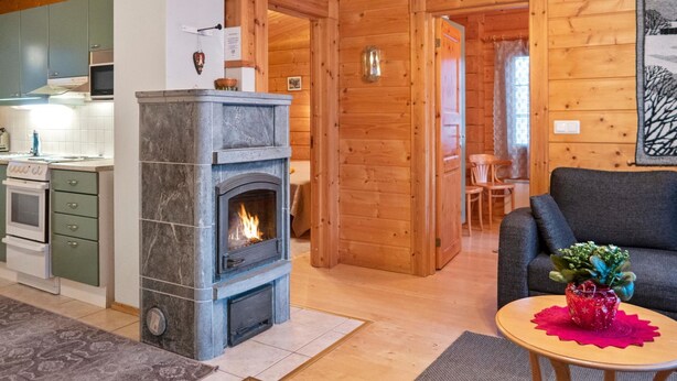 L’intérieur chaleureux d’un chalet avec une cheminée en pierre, des murs en bois, un coin repas et un salon comprenant un canapé et une petite table.