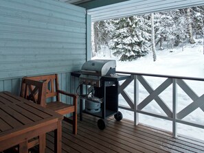 En träaltan med en grill och en stol, med utsikt över ett snötäckt landskap.
