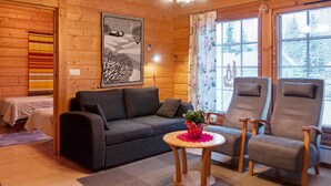 L’intérieur d’un chalet accueillant, avec un canapé, deux fauteuils, une petite table agrémentée d’une plante et une fenêtre équipée de stores.