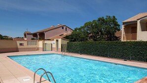 A rectangular swimming pool with a metal ladder on one side, surrounded by a tiled deck.