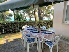 An outdoor dining area with a table set for four, surrounded by white chairs with blue cushions, under a green umbrella. - Tondini by Interhome (Pedaso)