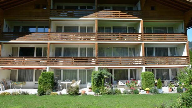 Un immeuble en bois à plusieurs étages, doté de balcons, de grandes fenêtres et d’un jardin bien entretenu.
