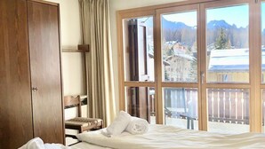 Habitación de hotel con dos camas, un armario de madera, una ventana con vistas a las montañas y una lámpara en el techo.
