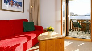 Una habitación con un sofá rojo, una mesa de centro de madera con un jarrón de flores, un cuadro en la pared y vistas a un paisaje nevado a través de una puerta corrediza de vidrio.