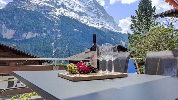 Ein Tisch mit einer Weinflasche, Gläsern und einer Obstschale, vor einer Bergkulisse.
