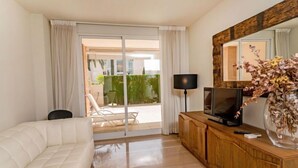 Une chambre d’hôtel moderne avec un canapé blanc, un meuble TV en bois, un téléviseur à écran plat, une lampe et un grand miroir.