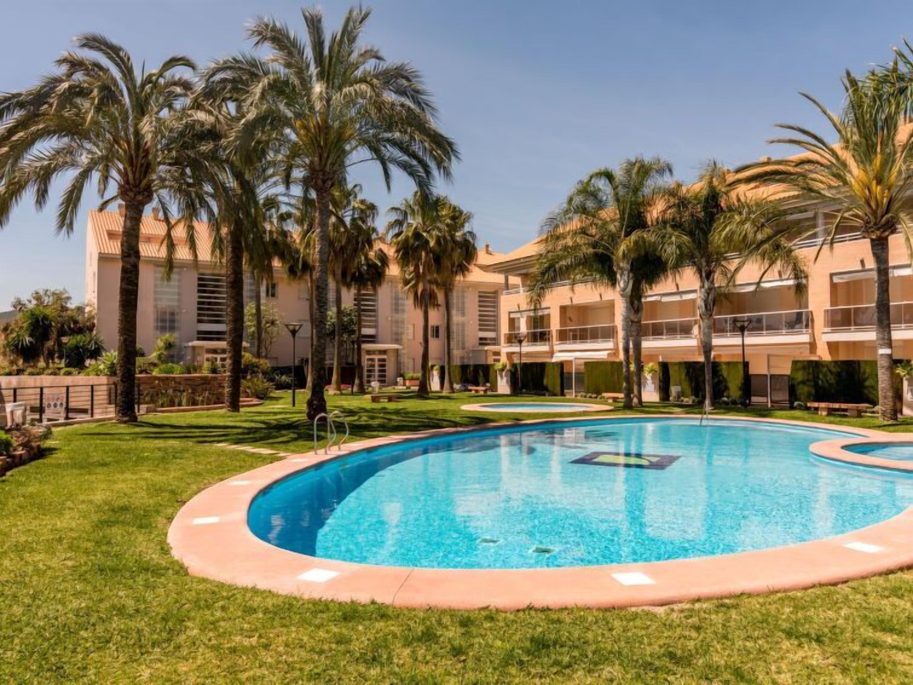 Una piscina rodeada de palmeras y un edificio de varios pisos con balcones.