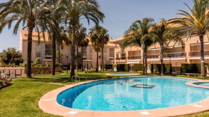 Une piscine entourée de palmiers et un immeuble à plusieurs étages doté de balcons.