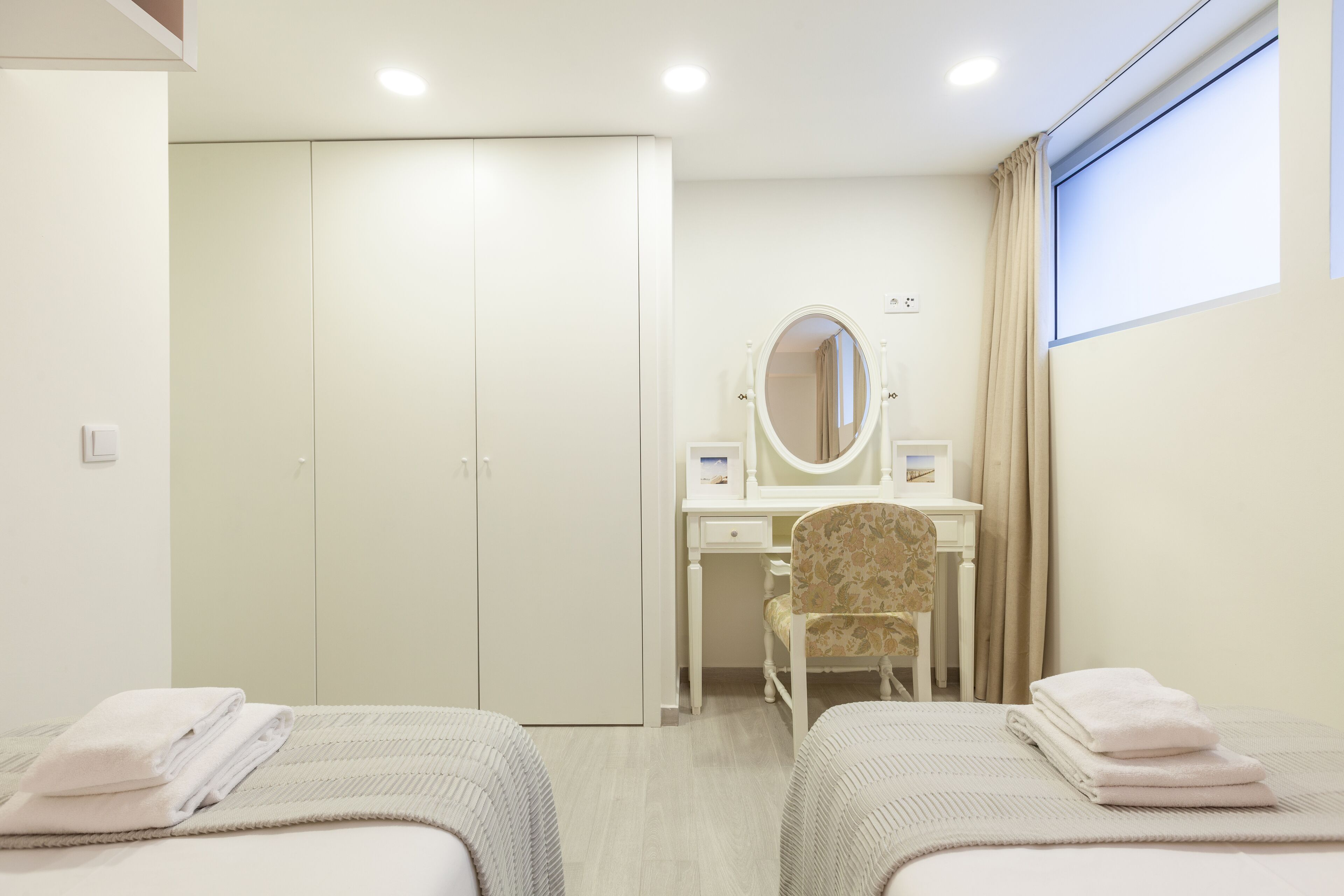 A hotel room with two beds, a desk with a chair, a wardrobe, and a window with curtains.