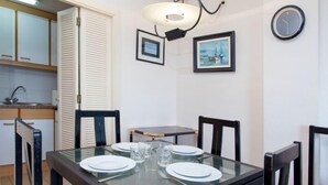 A dining area with a glass table set for four, surrounded by chairs. There is a small round table with two chairs, a clock on the wall, and framed pictures. - Windsor by Interhome (Blanes)