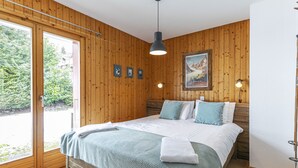 A bedroom with a wooden paneled wall, a bed with a green blanket, a painting, and a door leading to a balcony. - Brocard by Interhome (Val-d'Illiez)