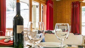 A dining area with a wooden table set for two, a bottle of wine, and red curtains. - Brocard by Interhome (Val-d'Illiez)