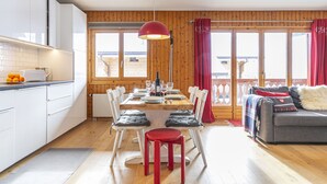 A modern kitchen with white cabinets, a dining area with a wooden table and chairs, and a cozy living area with a sofa and a blanket. - Brocard by Interhome (Val-d'Illiez)