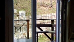 An open door leading to an outdoor deck with a wooden picnic table and a stone wall in the background. - Ferienwohnung Teufelsmauer Waldhaus (Blankenburg)