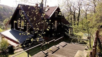 A wooden house with a sloped roof, surrounded by trees and a wooden deck.