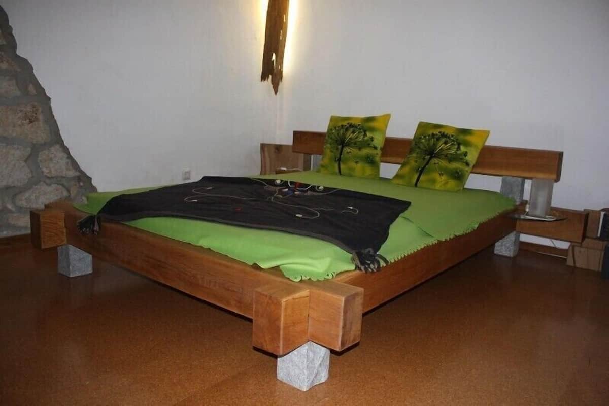 A bed with a green bedspread and two pillows with tree designs, a wooden headboard, and a stone accent wall.