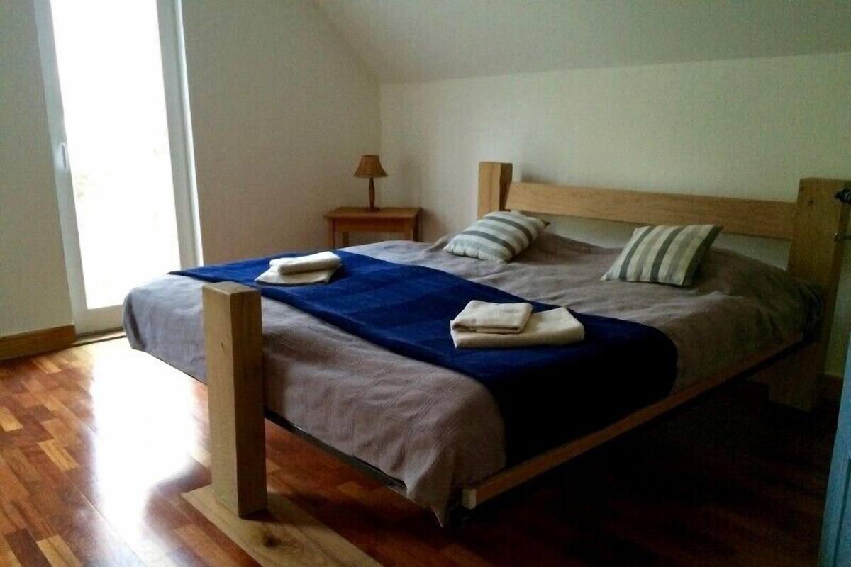 A single bed with a wooden frame, a blue bedspread, and two pillows.