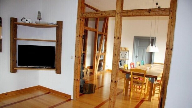 A room with exposed wooden beams, a wooden floor, a TV mounted on the wall, and a dining area with a table and chairs. - Ferienwohnung Teufelsmauer Waldhaus (Blankenburg)