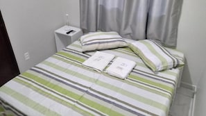 Una cama bien tendida con ropa de cama a rayas, una almohada y dos toallas dobladas.