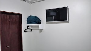 A room with a wooden door, a white wall-mounted shelf with a black hanger, and a flat-screen TV. - Pousada Pai Nosso (Aparecida)