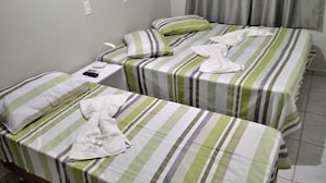 A hotel room with two single beds, each with striped bedding and pillows. There is a bedside table with a remote control and a phone. - Pousada Pai Nosso (Aparecida)