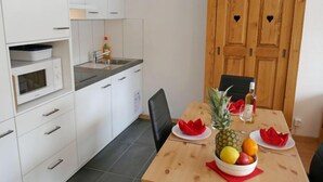 A compact kitchen with white cabinets, a microwave, and a sink. There's a wooden table with a fruit bowl and a bottle of olive oil.