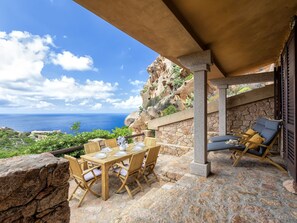 A covered outdoor dining area with a table set for two, stone walls, and a view of the ocean.