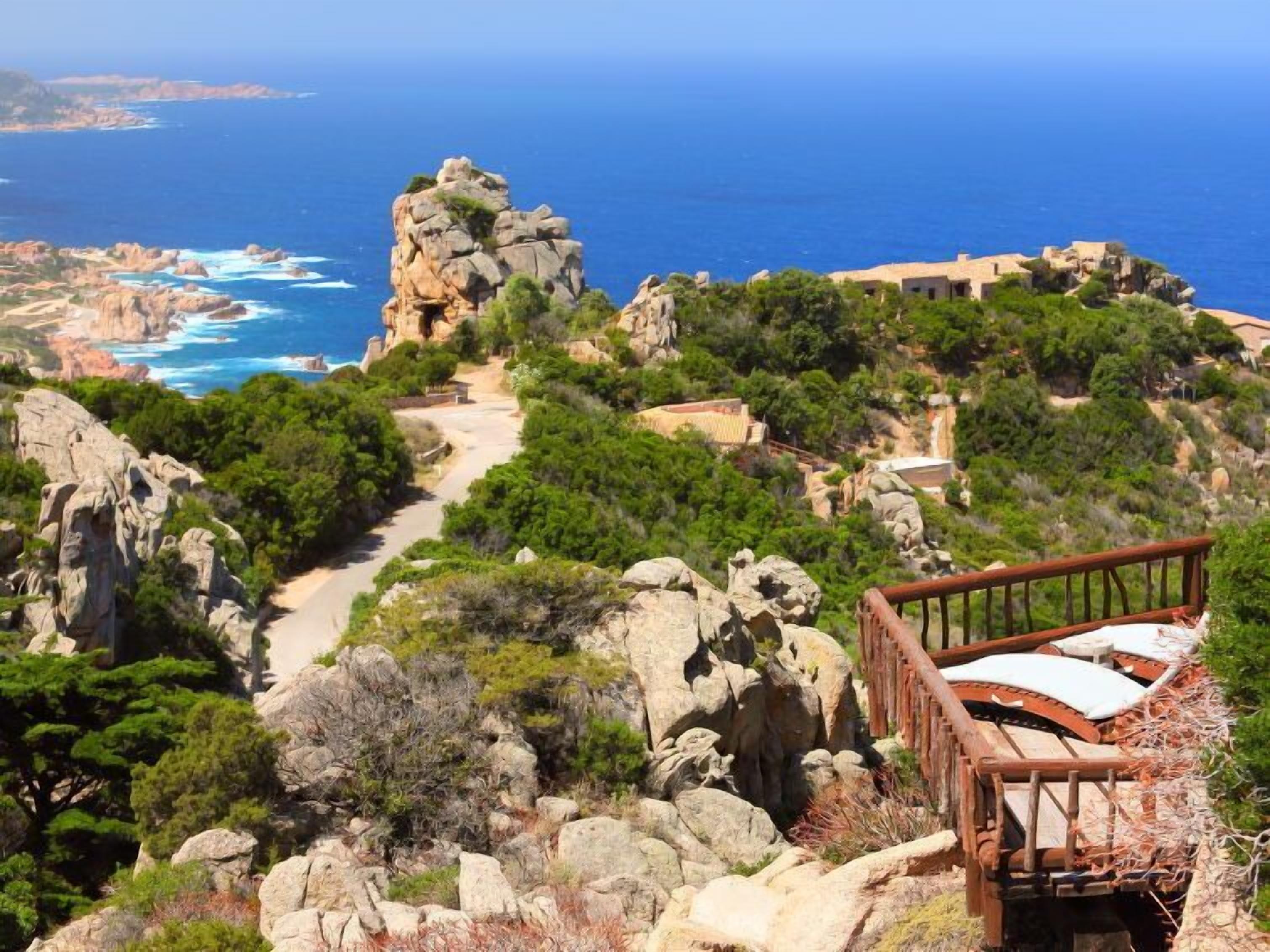 A coastal landscape with a rocky path leading to a wooden viewing platform overlooking the sea.