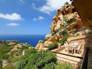 A coastal property with a stone staircase leading to a patio with outdoor furniture.