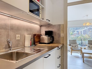 A modern kitchen with a built-in oven, a coffee machine, and a view of a balcony with outdoor seating.