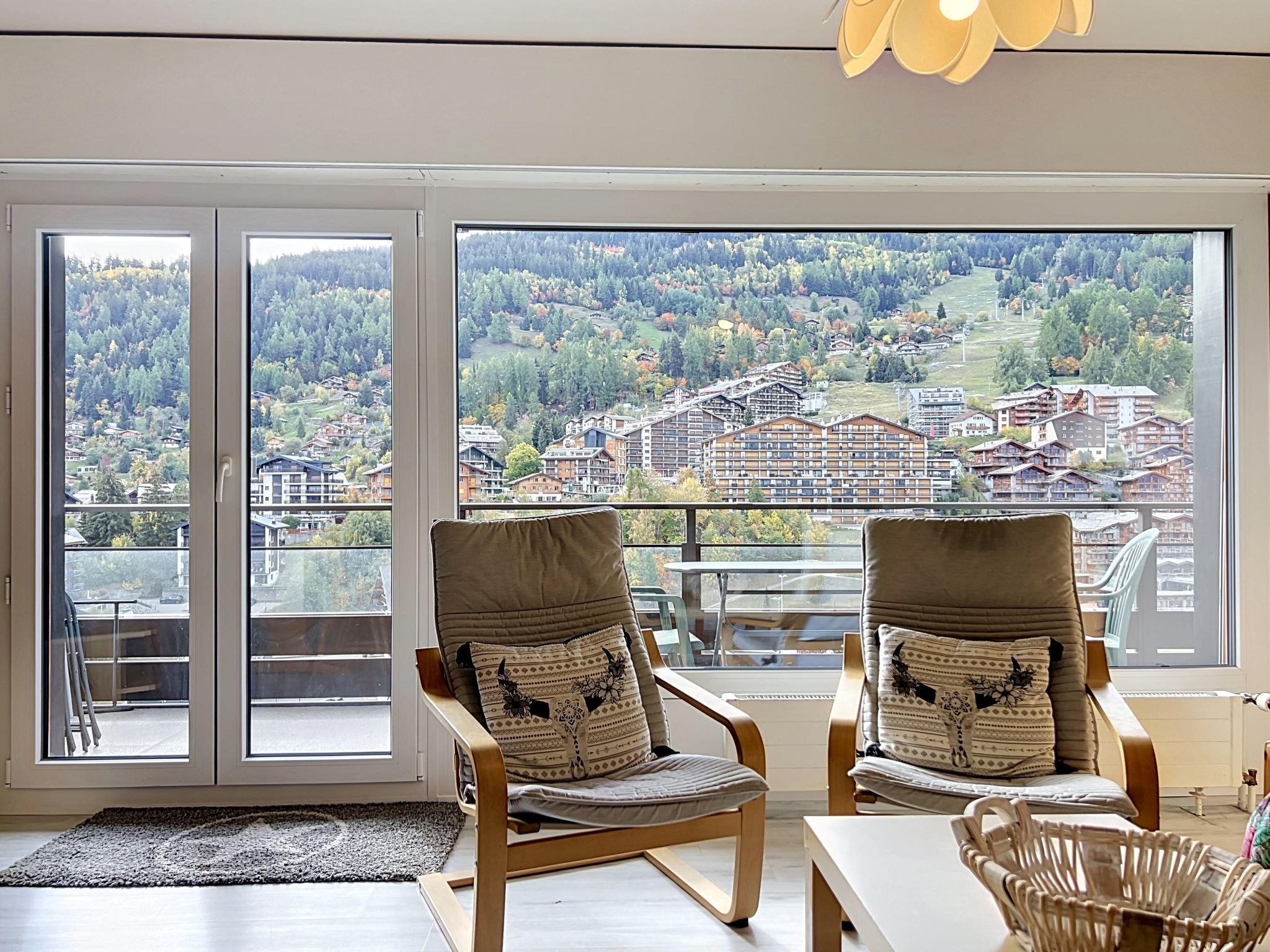 Une pièce avec deux fauteuils placés face à une grande fenêtre donnant sur un quartier résidentiel.