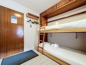 A bunk bed room with a wooden ladder, a door with a notice, and a small shelf with hangers.