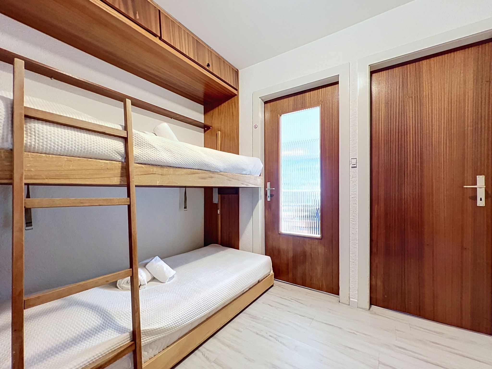 Ein Schlafzimmer mit Etagenbett, Holz Kopfteil, einem Einzelbett und einer Tür mit Fenster.