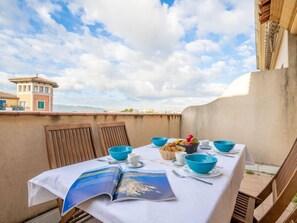 A table set for breakfast with blue bowls, a basket of bread, and a magazine on a balcony with a view of buildings and a cloudy sky. - Port Quiétude by Interhome (Fréjus)