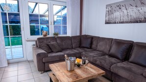 Un salon moderne avec un canapé d’angle, une table basse en bois et une grande fenêtre donnant sur l’extérieur.