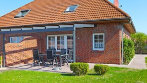 Une maison à deux étages, avec un toit recouvert de tuiles rouges, une façade en briques et un patio couvert aménagé avec du mobilier d’extérieur.